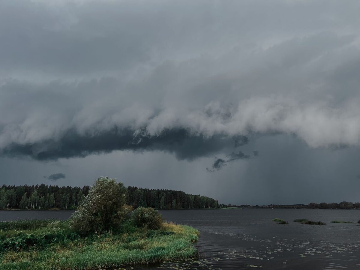A powerful storm cloud formation looms over a tranquil lake and forest, capturing nature's dynamic beauty.